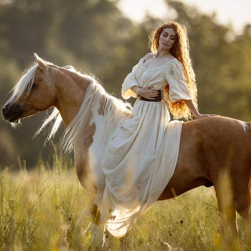 Woman in white dress sitting on brown horse in sunlit field