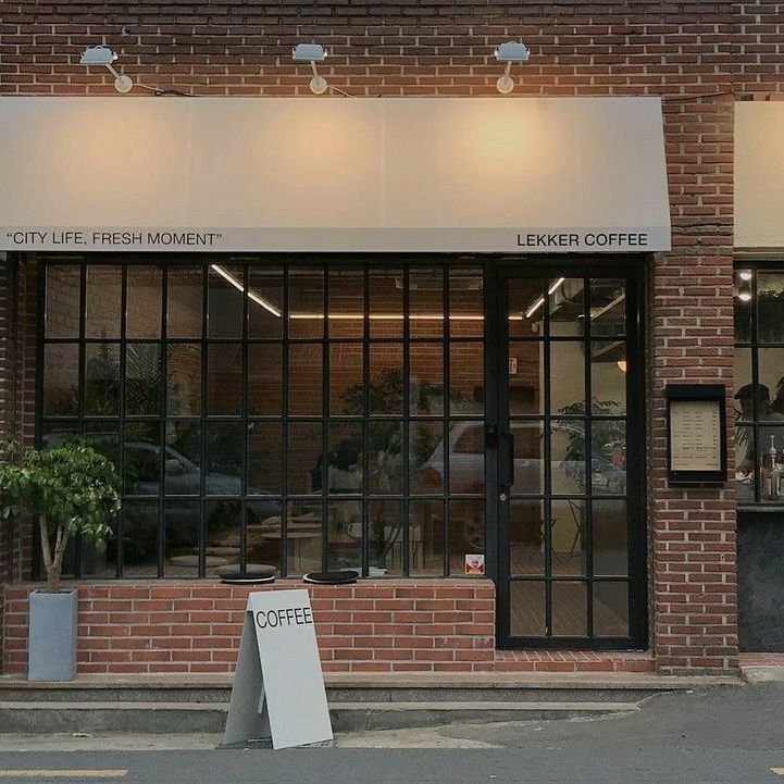 Modern brick cafe storefront with large black windows, potted plants, and a sidewalk sign