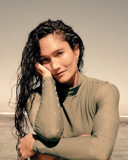 Woman with wet hair in a wetsuit posing by the ocean on a beach