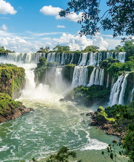 Panoramic view of Iguazu Falls with multiple cascades, green vegetation, mist, and blue sky