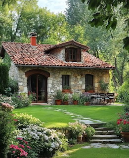 Stone cottage with red tile roof surrounded by green lawn and colorful garden beds