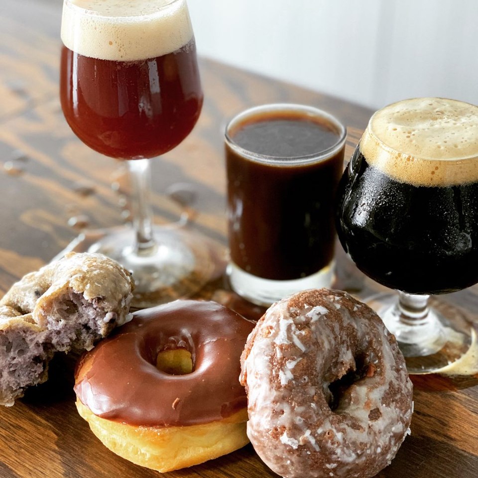 Three craft beers and assorted donuts arranged on a wooden table