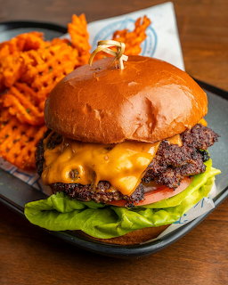 Cheeseburger with lettuce and tomato on brioche bun alongside sweet potato waffle fries on a plate