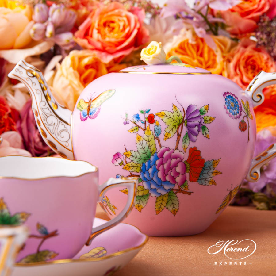 Pink porcelain teapot with colorful floral design surrounded by orange and pink roses