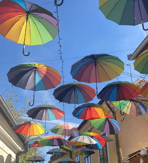 Rainbow umbrellas hanging over street in Szentendre, Hungary with blue sky and buildings