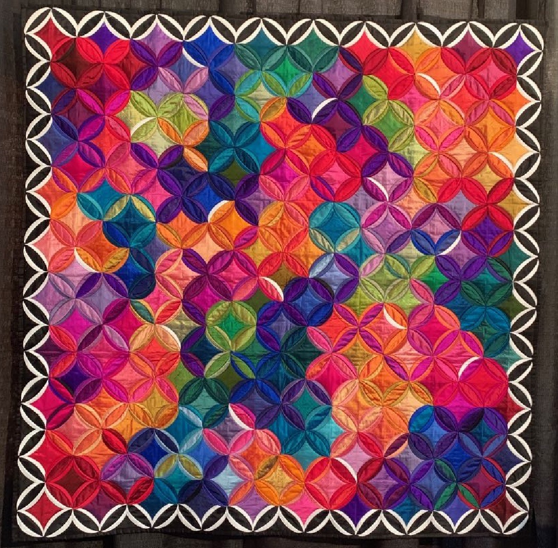Colorful patchwork quilt with interlocking geometric circle patterns in rainbow hues and white scalloped border