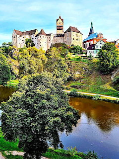 Medieval castle on hilltop overlooking river with green trees and blue sky