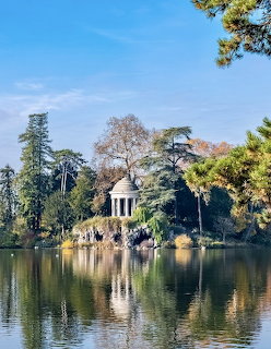 Classical pavilion by a lake with tree reflections and blue sky
