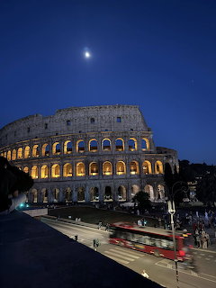 Illuminated Colosseum at night in Rome with the moon above and traffic on the street below