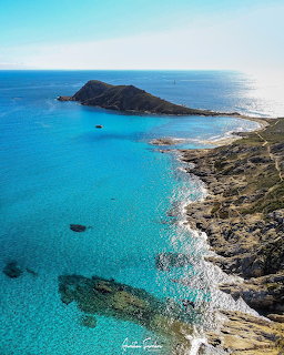 Rocky coastline and small island in clear turquoise ocean under a blue sky