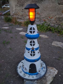 White and blue decorative lighthouse with glowing orange lamp on garden ground
