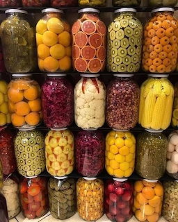 Shelves of glass jars containing colorful pickled vegetables and preserves