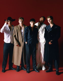 Five young men in stylish coats and suits posing against a red background