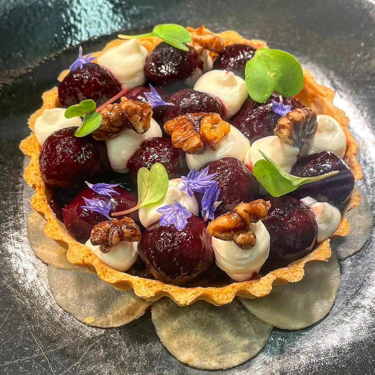 Tart with roasted beetroot, white drizzle, walnuts and purple flowers on silver plate