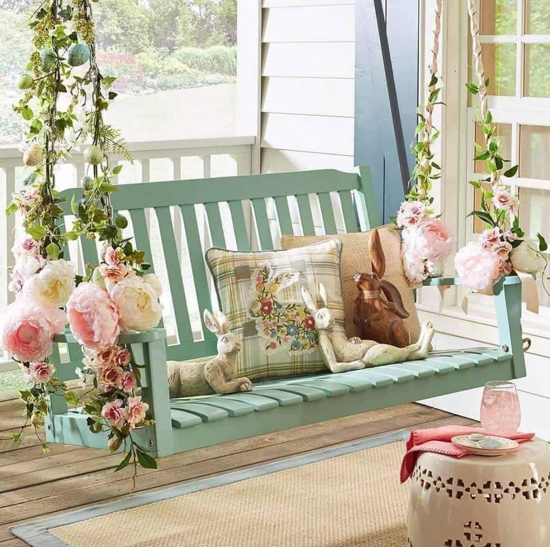 Turquoise porch swing with pink flowers, pillows, and decorative bunny on wooden deck