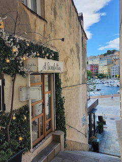 Narrow alley by a stone building leading to a harbor with boats and waterfront buildings in Corsica