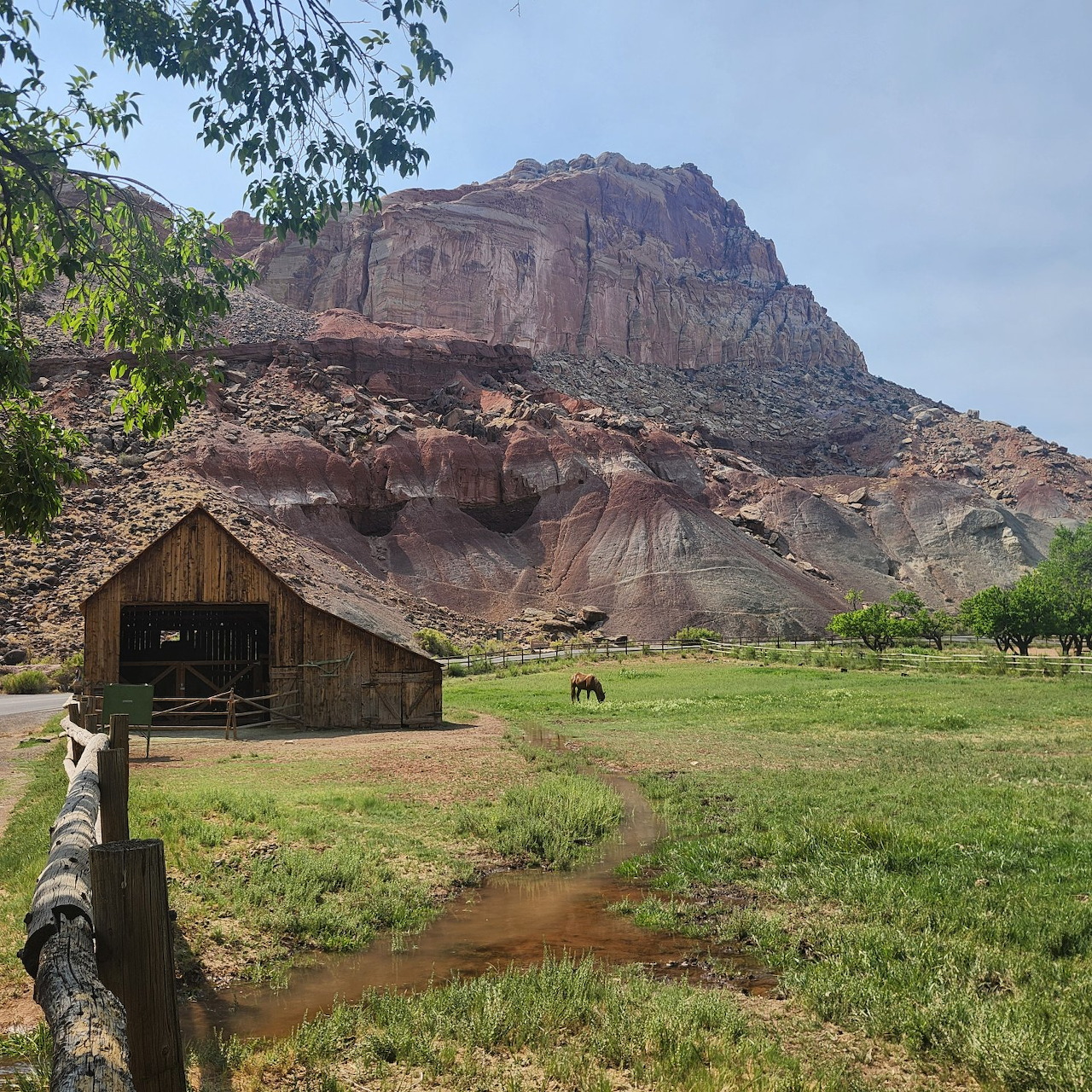 Wooden barn in a grassy field with red rock cliffs and cloudy sky