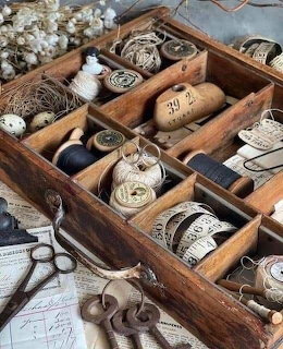 Vintage wooden sewing drawer with compartments holding thread spools, twine, scissors, and measuring tapes