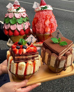 Four elaborate miniature dessert cakes with strawberries, chocolate, and fruit toppings arranged on a wooden serving board