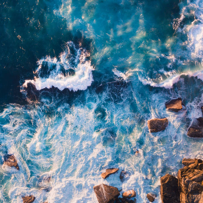 Aerial view of ocean waves breaking on rocky shore with white foam and turquoise water