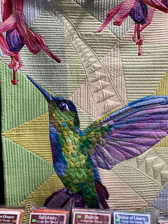 Close-up of a colorful quilted hummingbird with purple flowers and geometric stitched fabric