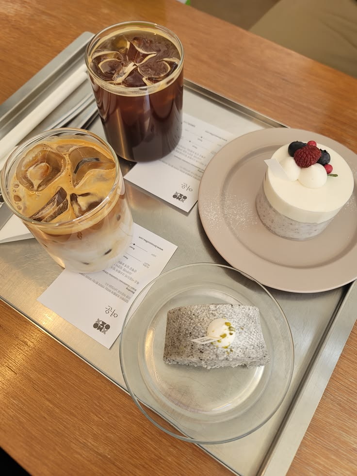 Cafe tray with iced latte, iced americano, a berry-topped cream cake, and a rice cake roll
