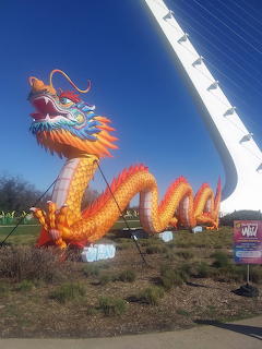 Large colorful dragon lantern sculpture outdoors with blue sky and bridge cables in background