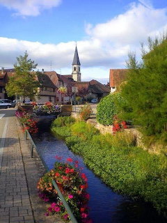 Scenic canal with colorful flowers, historic buildings, and church steeple in European village