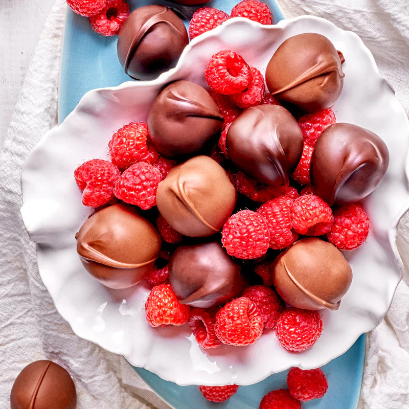 Chocolate-covered raspberries on white plate with blue placemat and linen cloth