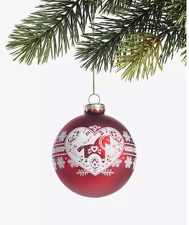 Red Christmas ornament with white heart design hanging from a pine branch on a white background