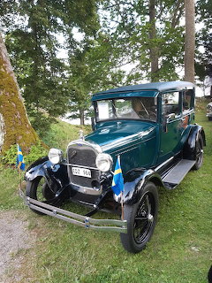 Vintage green Ford Model A car parked on grass with a Swedish flag near trees