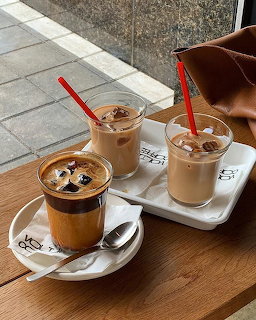 Three iced coffee drinks on trays on a wooden table by a window