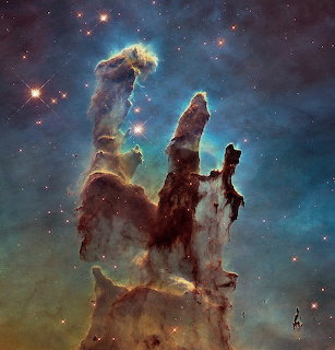 Towering cosmic gas pillars in teal and brown hues with bright stars against a nebula backdrop
