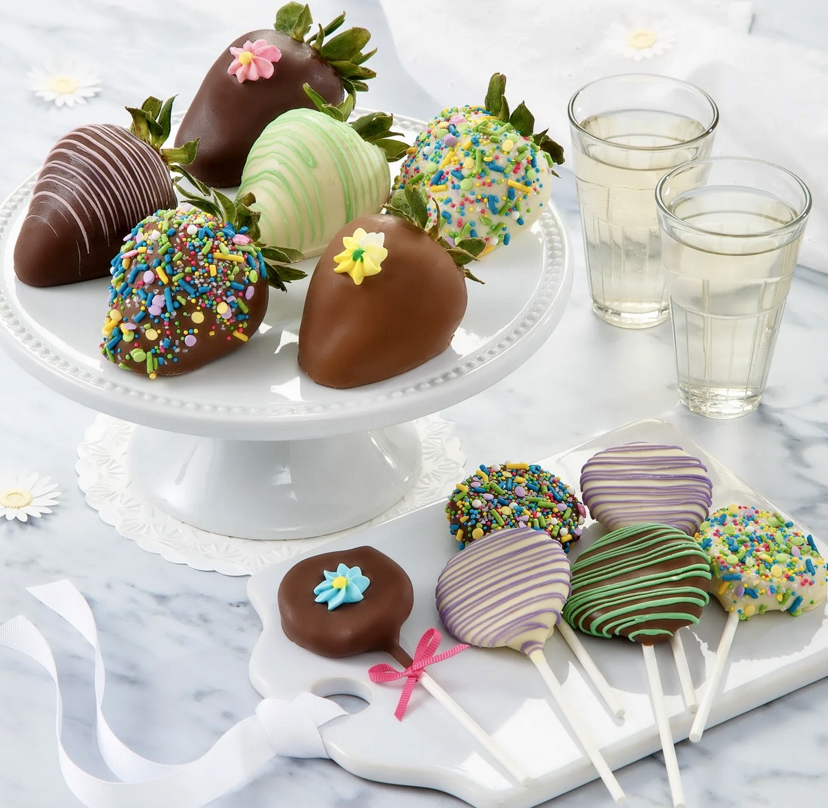 Chocolate-covered strawberries and cake pops with sprinkles on white serving platters