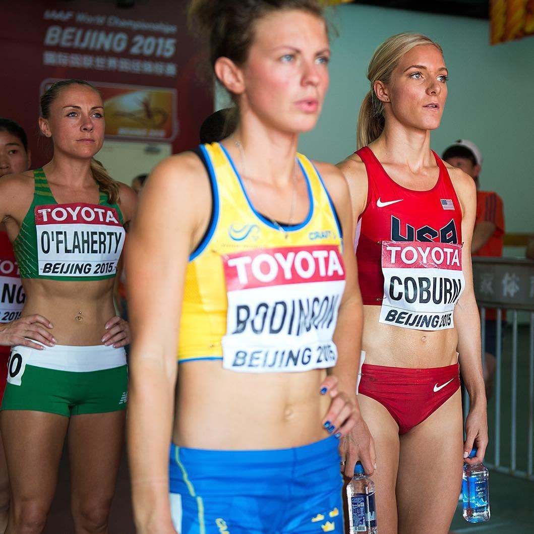 Three female athletes in athletic uniforms with numbered bibs at a track competition
