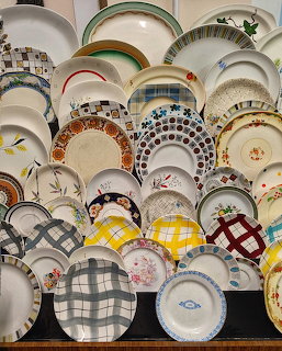 Wall display of assorted vintage decorative plates with floral and plaid patterns in various colors