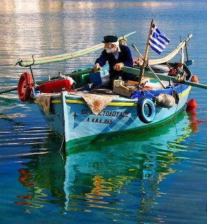 Greek fisherman on a colorful traditional wooden boat with Greek flag in calm harbor waters