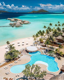 Aerial view of tropical resort with pool, beach, palm trees, and turquoise ocean