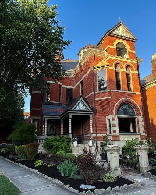 Ornate Victorian red brick mansion with arched windows and landscaped front garden on a sunny day