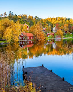 Red lakeside houses reflected in a calm lake with a wooden dock and golden autumn trees