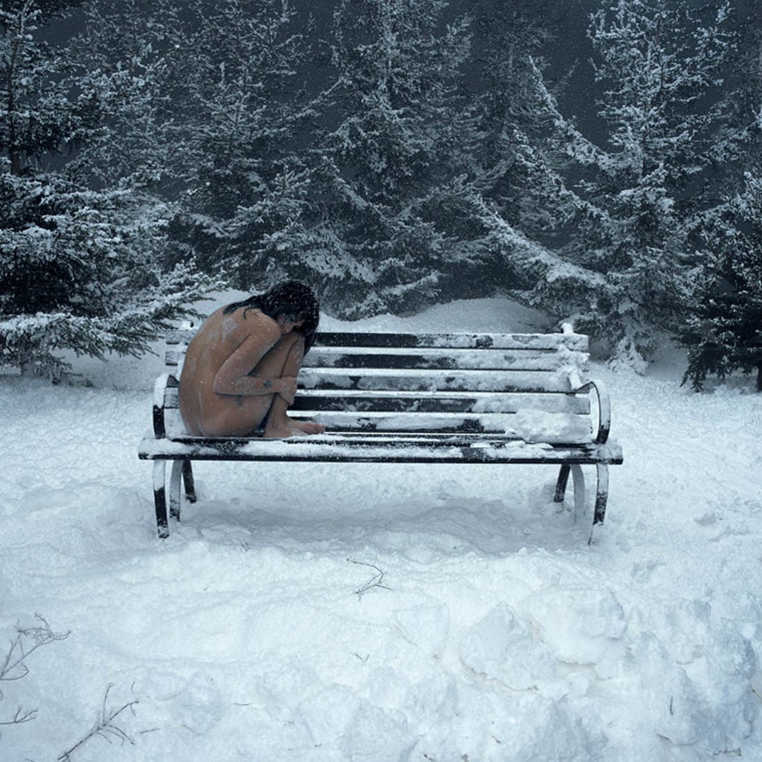 Woman sitting on wooden bench in snowy winter forest with evergreen trees