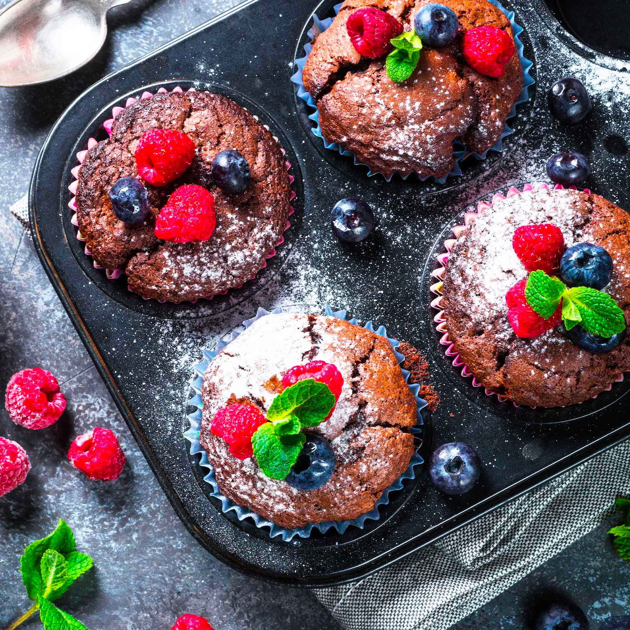 Four chocolate lava cakes topped with raspberries, blueberries and mint on a baking pan