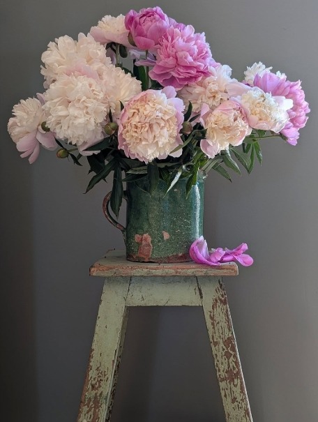 Pink and white peony bouquet in a green vase on a weathered stool