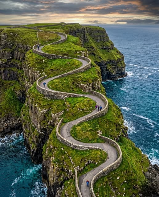 Winding narrow road descending steep green cliffs to Dunquin Pier on the Irish coast with ocean waves below