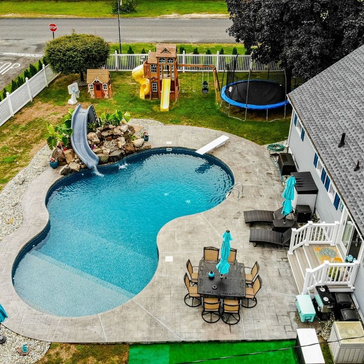 Aerial view of a backyard swimming pool beside a house with patio furniture, playset, and trampoline