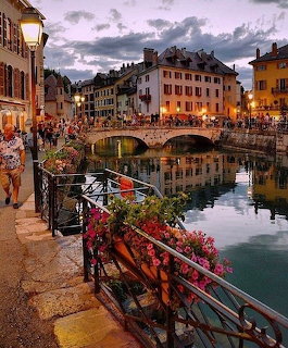 European canal town at dusk with stone bridge, old buildings, flowers, and warm reflections on water