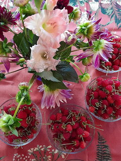 Bouquet of pink flowers with glass bowls of fresh raspberries on a pink tablecloth