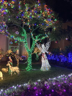 Outdoor Christmas light display with glowing angel, reindeer, decorated tree and colorful LED lights at night