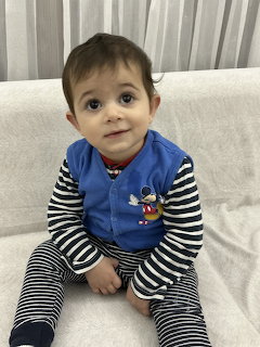 Toddler sitting on a light sofa in a blue vest and striped clothes, looking up at the camera