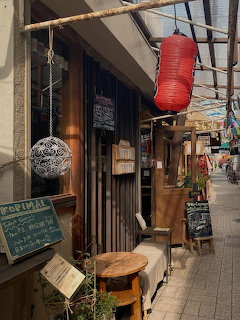 Small coffee shop in a narrow Osaka alley with stools, chalkboard signs, and a red lantern